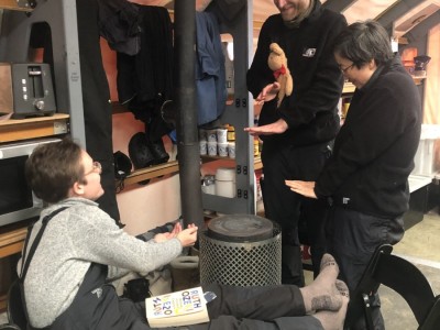 Scientists Linda Balfoort, Arne Ulfers, and Jae Il Lee warm themselves around the stove in the mess tent on a cold and windy day.